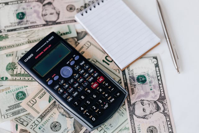 A calculator and a notepad on top of some American money.