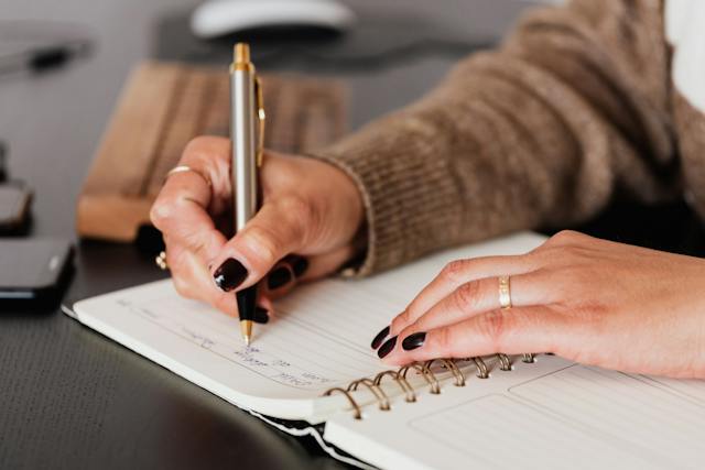 The hands of a person writing in a notebook.