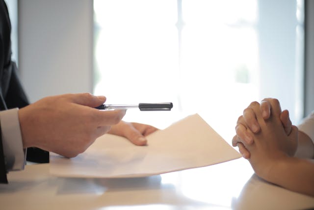One person handing another person a contract over a table.